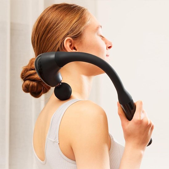 Femme rousse yeux fermés appliquant pistolet de massage sur dos